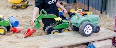 A cropped photo of a child playing with a toy truck in the sand.